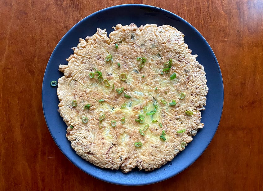 1/2 cup all-purpose flour 6 eggs, lightly beaten 1 tablespoon vegetable oil, plus more for frying 5 scallions (green parts only), cut into 3-inch pieces and sliced lengthwise 5 to 6 cups shredded green cabbage 1 cup mayonnaise 1 canned chipotle and a little of its adobo sauce Salt and pepper